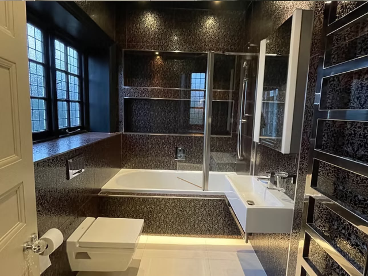 Bathroom finished in dark mosaic tile with a panelled bath, walk-in shower and heated towel rail.