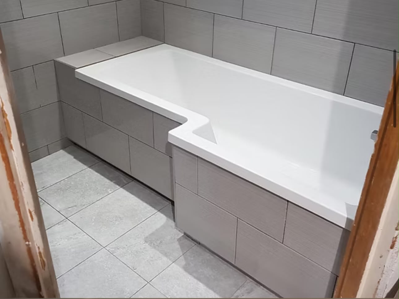 Bathroom with a panelled bath and large-format grey wall and floor tiles.