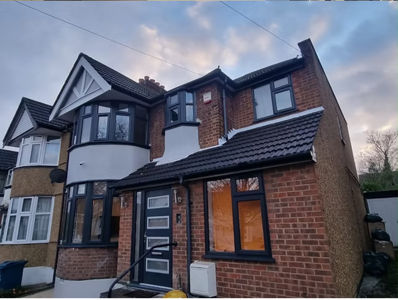 Semi-detached house at dusk with new black-framed windows and a freshly rendered white upper storey.