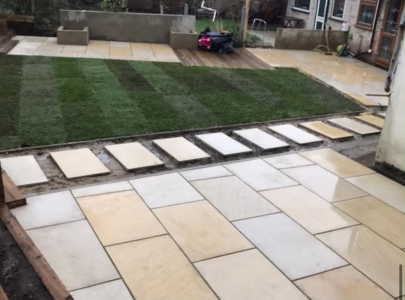 Rear garden mid-build with fresh turf, sandstone paving slabs and a new retaining wall.