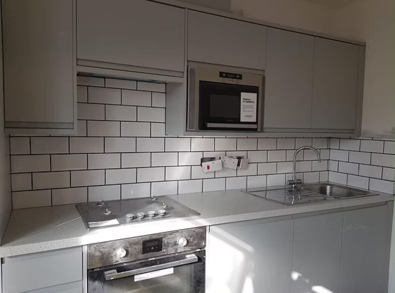 Fitted kitchen with handleless grey units, a metro-tile splashback and an integrated oven and microwave.