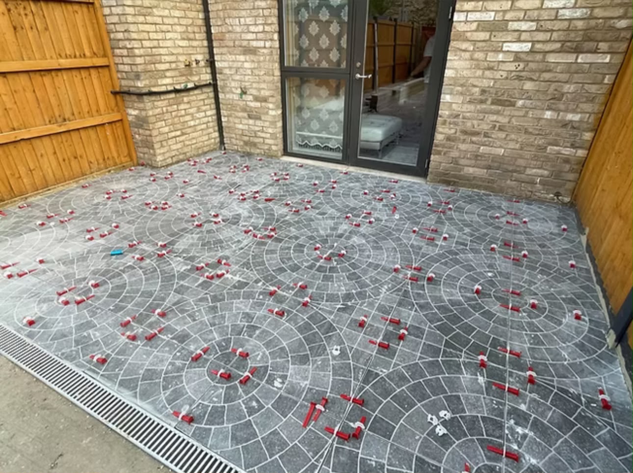 Circular-pattern patio part-laid with spacers still in place, enclosed by new brick walls.