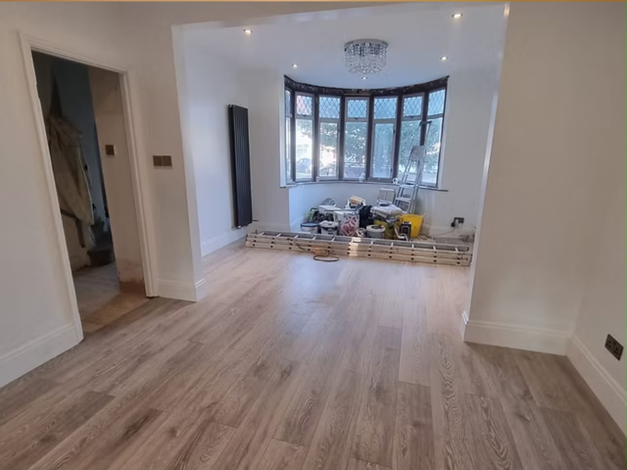 Through reception room after refurbishment, with new wood-effect flooring, fresh plaster and a bay window.